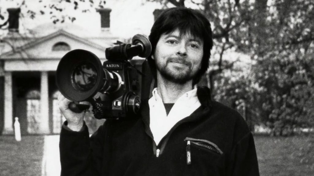 A young Ken Burns holds a large video camera on his shoulder.