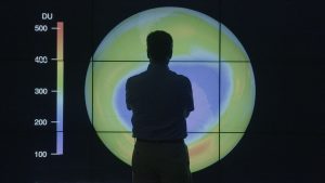 A man stands before a large screen displaying a temperature reading, highlighting the importance of climate awareness.