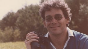 Raul Julia holds a set of binoculars