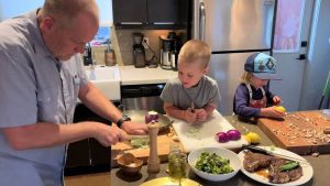 Father cooking with his two young sons in the kitchen by preparing vegetables.