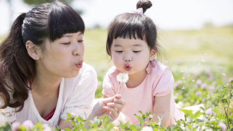 A woman and little girl blow a dandelion
