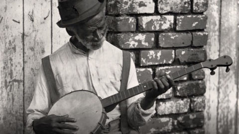 An elderly black man playing a banjo