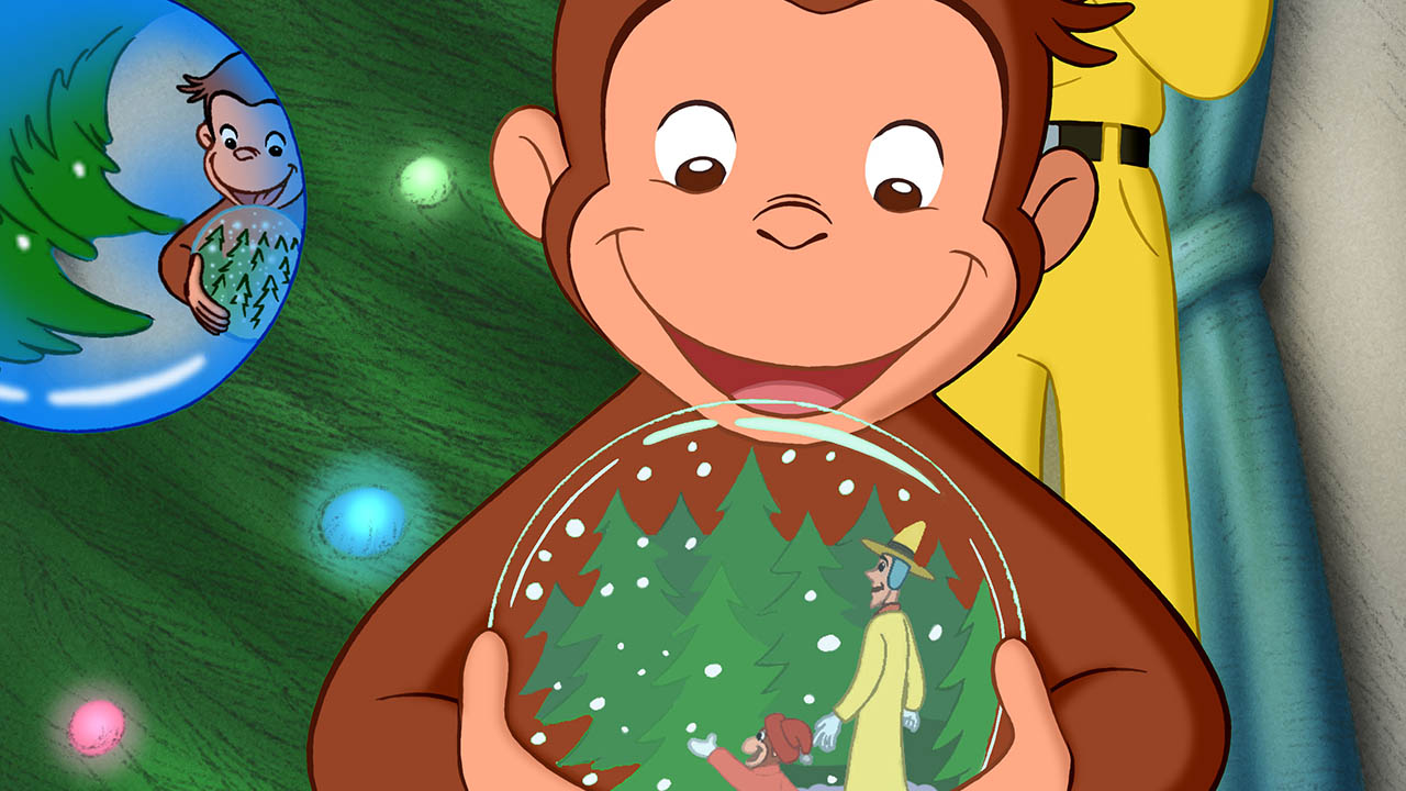 Curious George holds a snow globe in front of the Christmas tree