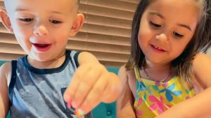 Two children add sprinkles to a craft project