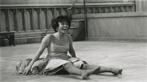 Rita Moreno in West Side Story, sits on the stage laughing.