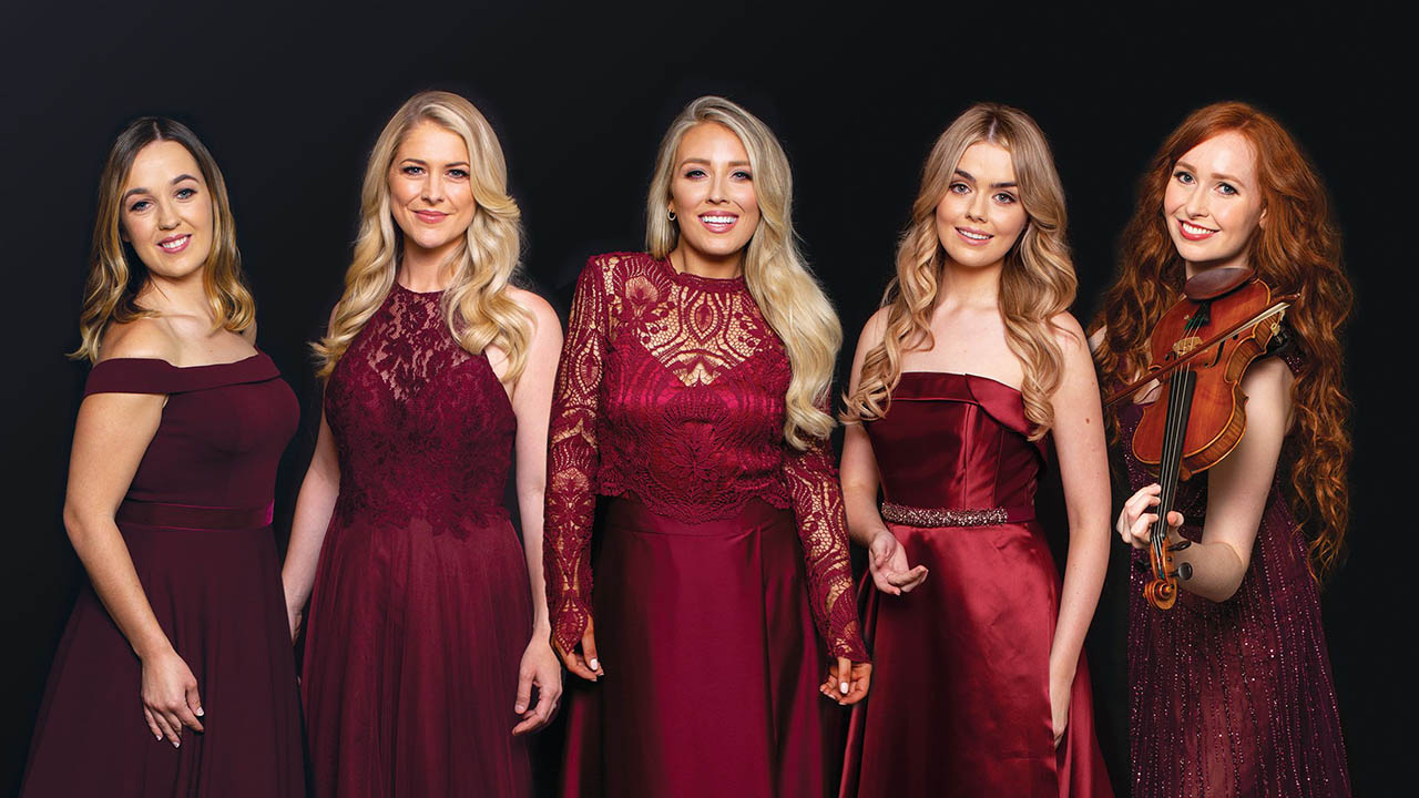 The five members of Celtic Woman pose together in dark red gowns.