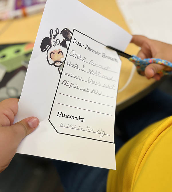 A child uses scissors to cut out a writing assignment.