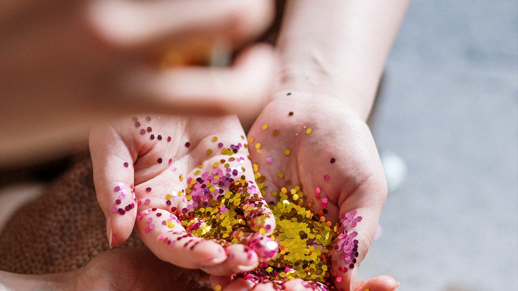 two hands holding specs of pink and gold glitter