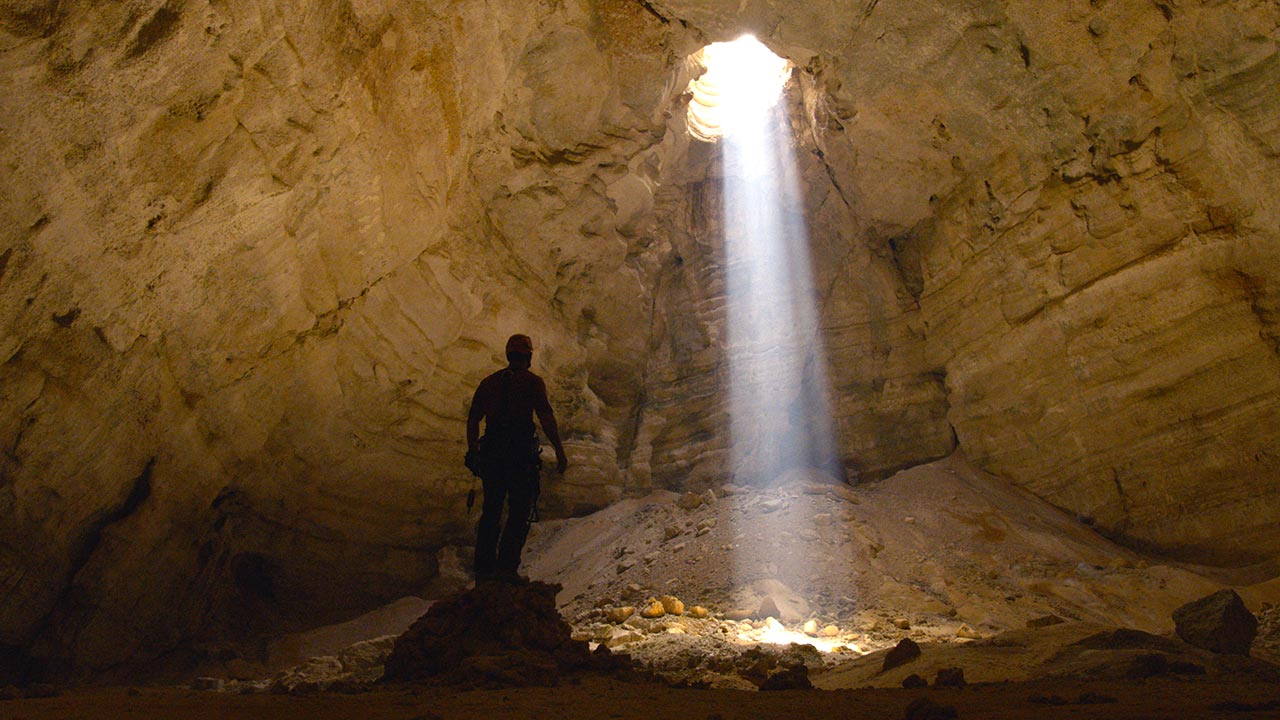 steve backshall looking at a beam of light in a cave