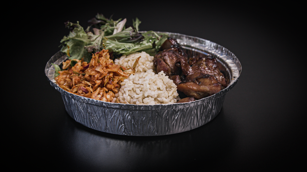 Chicken, steak, rice, and greens sit in a tin bowl on a table