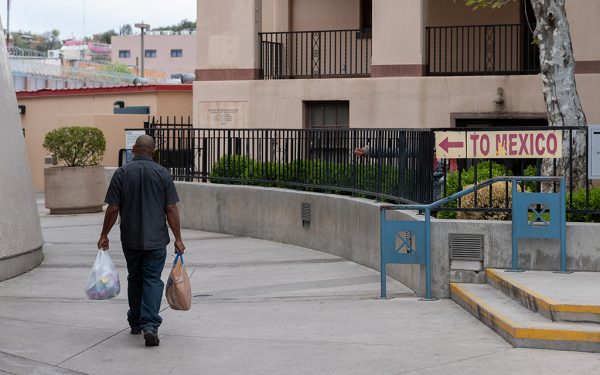 A man carrying shopping bags walks toward the border of Nogales