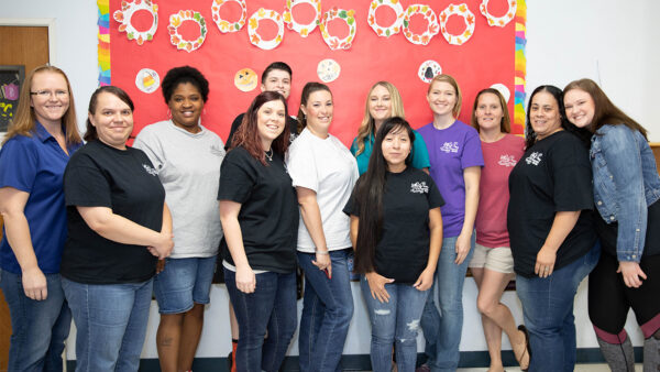 A class of early childhood educators poses together in front of a bulletin board