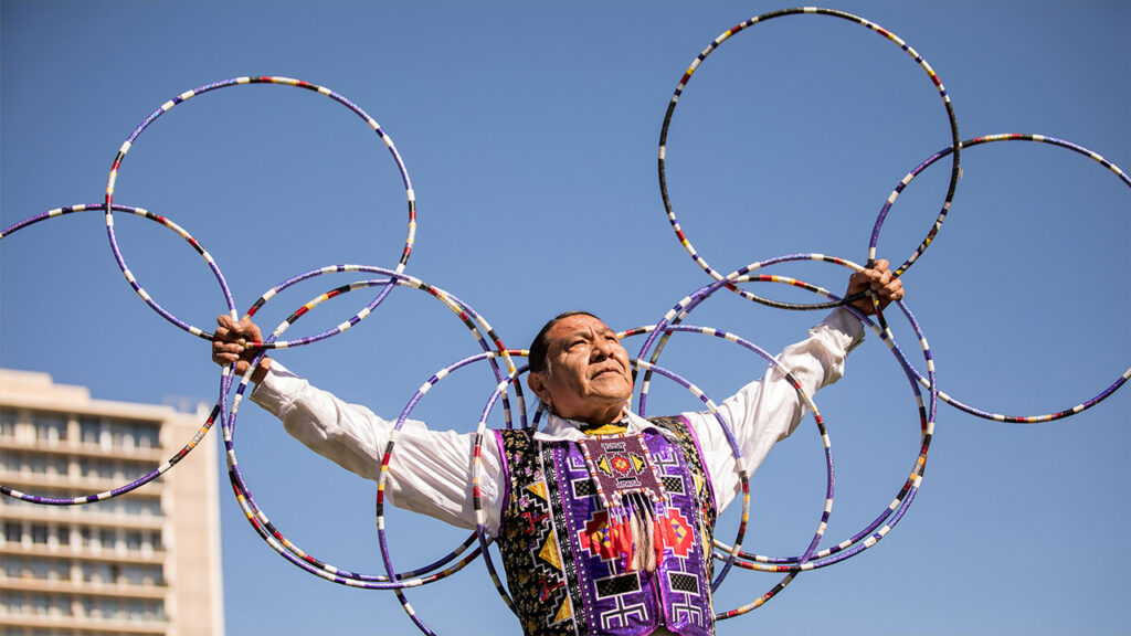 A hoop dancer creates an intricate pattern of hoops across his arms