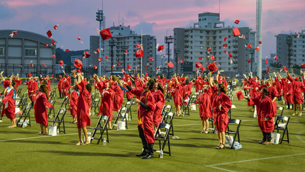 High school students in red robes toss their caps at graduation.