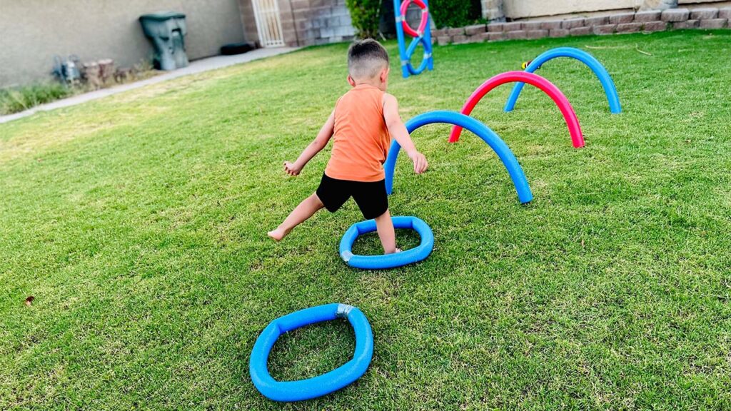 A child jumps through pool noodle hoops