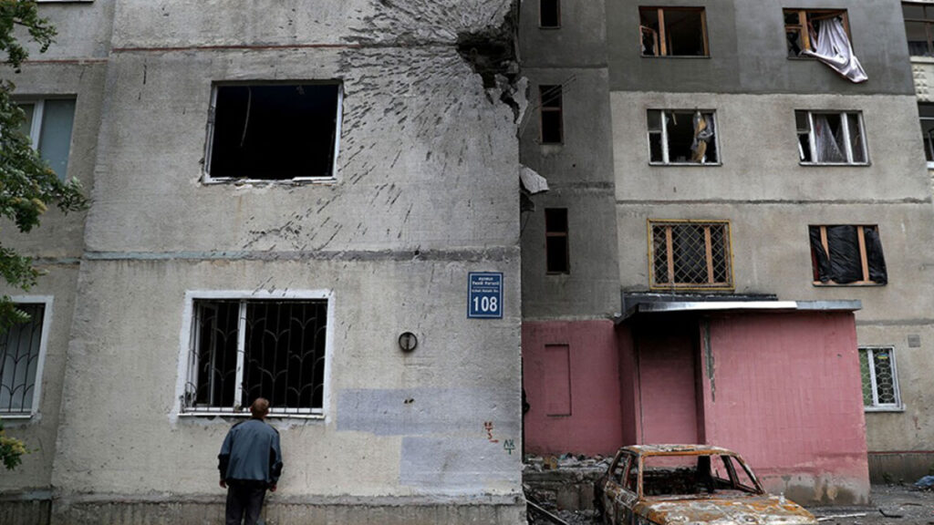 A man in Ukraine looks above at a shelled building