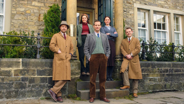 The cast of All Creatures Great and Small poses in front of a building