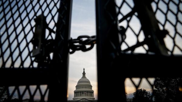 The dome of the U.S. Capitol building is visible through the gap in a fence secured with a chain.