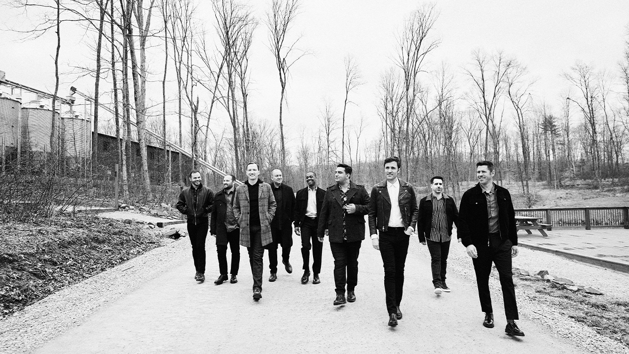 The nine vocalists of Straight No Chaser walk down a deserted road