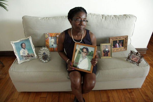 A black woman sits on a couch surrounded by framed photos