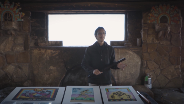 photo of a man showcasing three different pieces of art work on the table in front of him