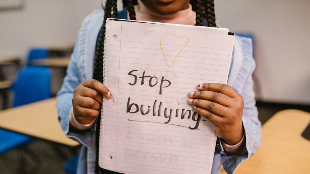 A Black girl holds up a notebook with the words Stop Bullying written on the page in large letters.