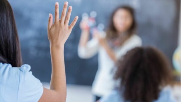 Photo shows a little girl on a classroom raising her hand