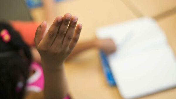Photo Shows a little girl raising her hand in a classroom