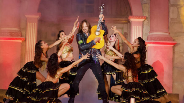 Benise performs on guitar, surrounded by dancers
