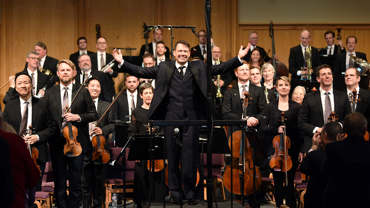 orchestra standing onstage facing audience