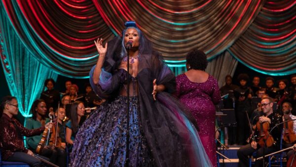 A singer performs on Broadway in a beautiful dress with an orchestra behind her