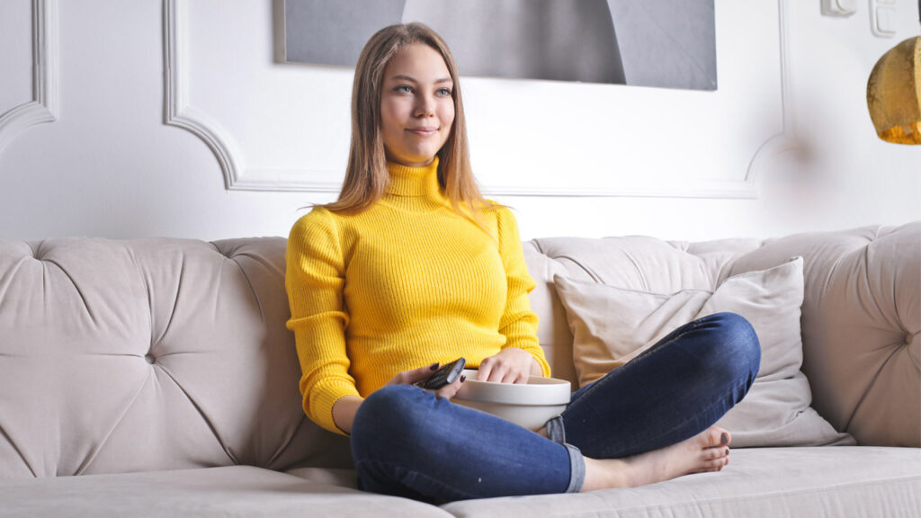 Woman in yellow sweater sits on couch watching tv