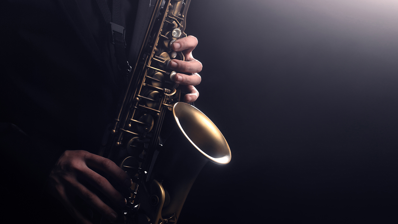 person playing saxophone against a black backdrop with dim lighting