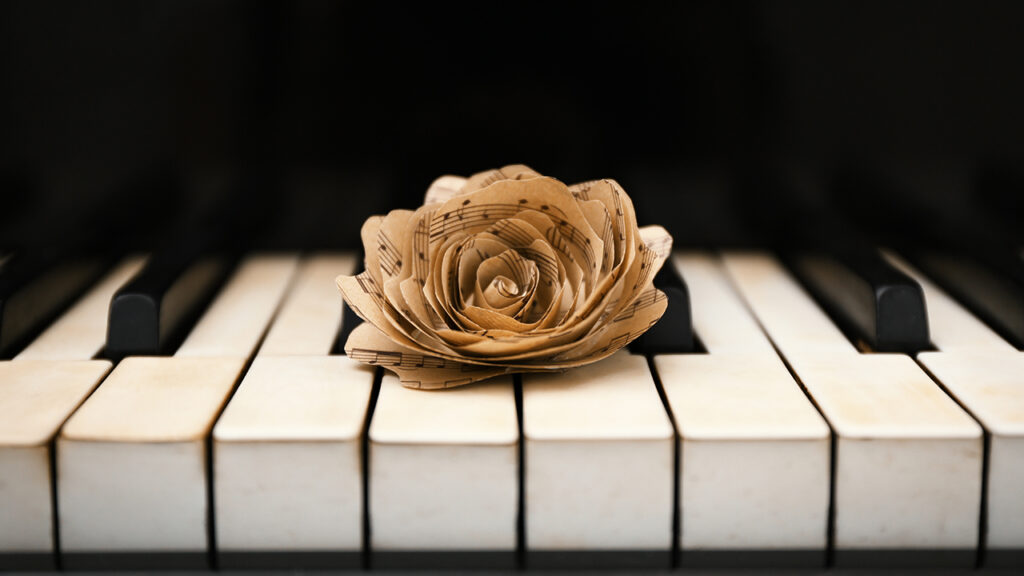 paper rose made of sheet music resting on piano keys