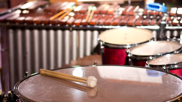 Percussion set up with a timpani in the foreground with a mallet resting on top. In the background are three toms and a marimba