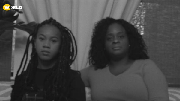 Two black women sit next to each other and look into the camera