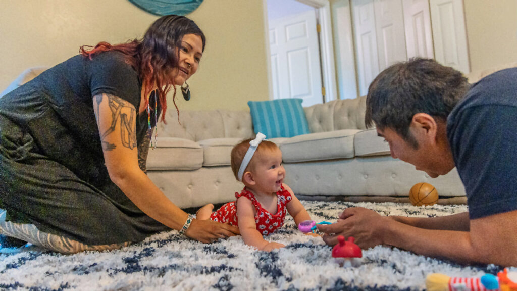A mother and father play with their baby during tummy time