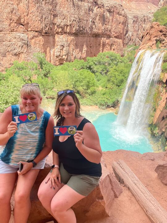 Two AZPBS Education team members pose in front of Havasupai Falls with PBS stickers.