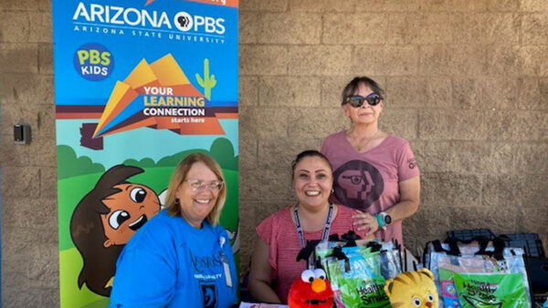 Women pose for a photo in front of the Arizona PBS education booth.