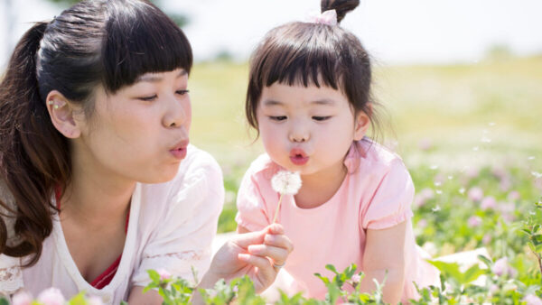 A woman and her young daughter blow on a dandelion.