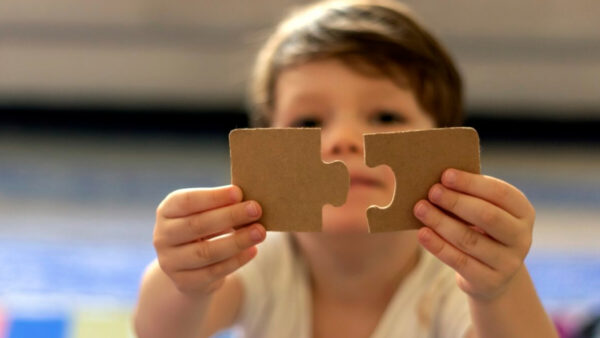 A child holds up two puzzle pieces that fit together.