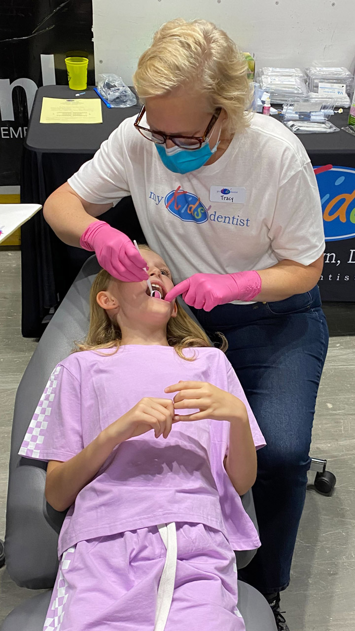 A young girl gets her teeth cleaned by a dental tech