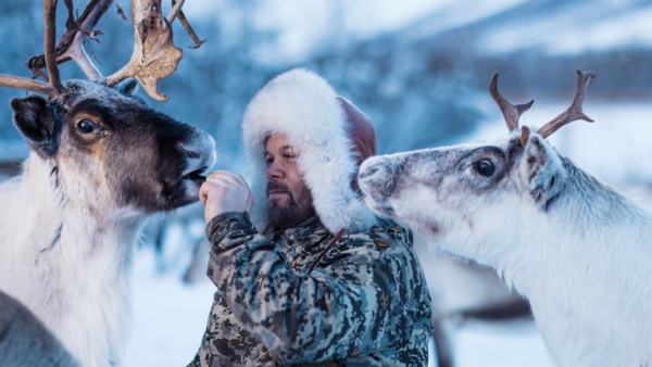 A man wearing a heavy coat feeds reindeer in the arctic on Evolution Earth on pbs
