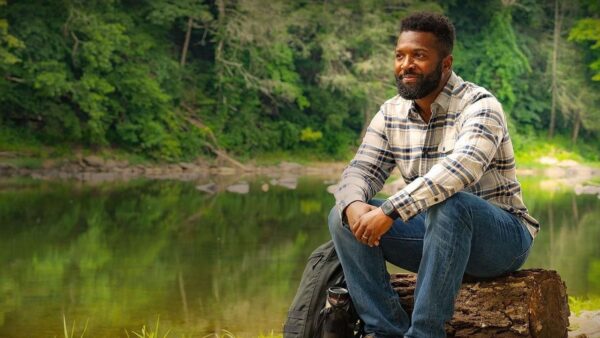 baratunde thurston sites on a wooden log next to a lake in Arkansas