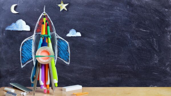 A rocket ship made out of craft materials like tape and pencils sits on a desk
