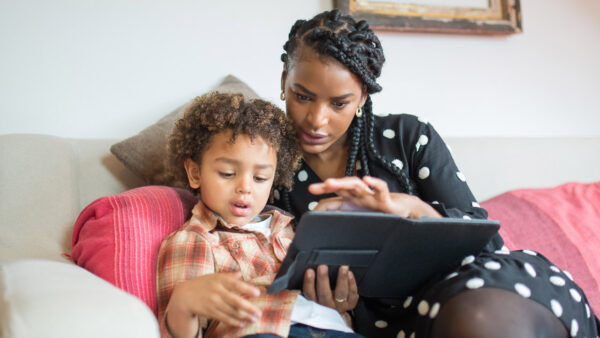 A mother and son sit on a couch looking at a tablet together