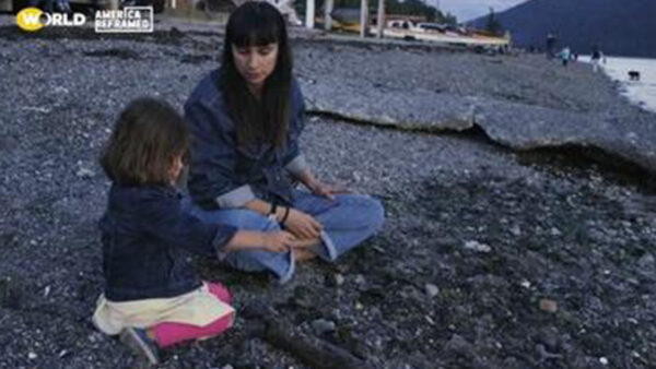A Native American mother sits with her daughter on a rocky beach
