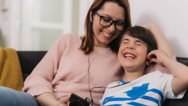 A mother and son sit on a couch and listen to a podcast.