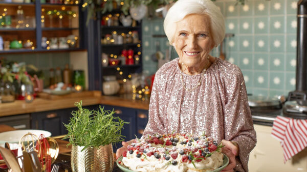 Mary Berry stands in a kitchen, smiles at the camera, and holds a plate of holiday treats from her new special, 