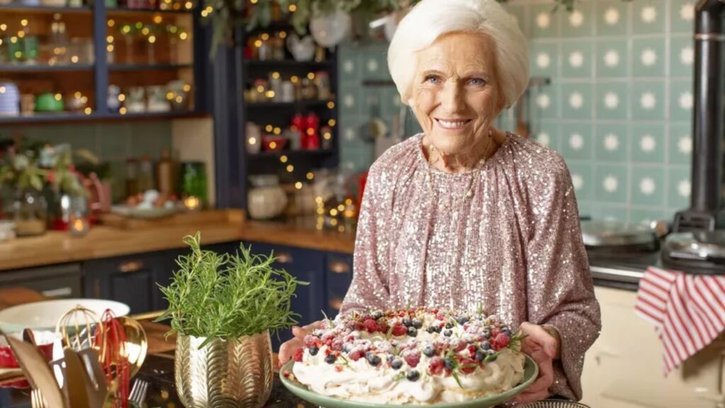 Mary Berry stands in a kitchen, smiles at the camera, and holds a plate of holiday treats from her new special, 